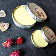 Lade das Bild in den Galerie-Viewer, Das Bild zeigt zwei geöffnete silberne Metalldosen mit gelblicher Schutz- und Pflegesalbe der Marke Fragantura. Auf den Deckeln steht "Popoflott – Schutz und Pflege" mit einer Illustration von einem lächelnden älteren Mann und einer älteren Frau. Die Dosen liegen auf dunklem Schiefer, umgeben von kleinen Herz- und Blüten-Elementen.