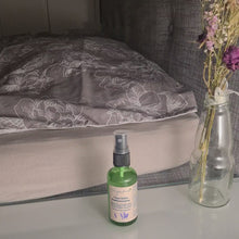 Laden und Abspielen von Videos im Galerie-Viewer, Zusehen ist ein Bett, Fokus auf das Kopfkissen, von der Seite. Davor ist ein Nachttisch, auf dem rechts eine Glasvase mit Trockenblumen und links davon das "Träum-Schön-Kopfkissenspray" zusehen ist. Eine Hand kommt von links in das Bild, nimmt die Kappe des Sprays ab, besprüht einmal das Kopfkissen, legt die Flasche auf dem Tisch ab und verschließt sie wieder mit dem Plastikdeckel. Das Video simuliert ein Abendritual.