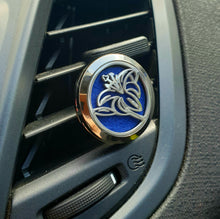 Lade das Bild in den Galerie-Viewer, Silberner Auto-Duftanhänger in Blumenform mit blauem Filzeinsatz, befestigt an einem schwarzen Lüftungsgitter im Fahrzeuginnenraum.