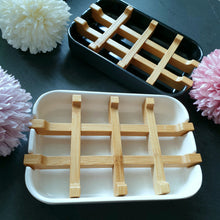 Lade das Bild in den Galerie-Viewer, Eine weiße und eine schwarze Seifenschale mit Bambuseinsätzen nebeneinander arrangiert, umgeben von vier pastellfarbenen Blüten.