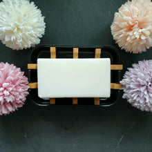 Lade das Bild in den Galerie-Viewer, Rechteckige, schwarze Seifenschale mit Bambuseinsatz, darauf ein weißes Seifenstück, umgeben von vier zarten, blütenförmigen Dekoelementen.