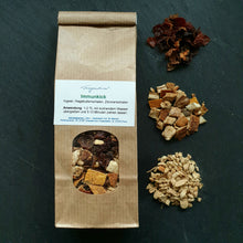 Lade das Bild in den Galerie-Viewer, Papiertüte „Fragantura Immunkick“ mit Sichtfenster, daneben drei kleine Häufchen sortierte Zutaten: oben Hagebutten, in der Mitte Zitrusschalen, unten Ingwerstückchen.