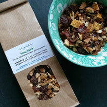 Lade das Bild in den Galerie-Viewer, Geöffnete Papiertüte „Fragantura Immunkick“ liegt neben einer grünen Schale, die mit der losen Teemischung gefüllt ist. Sichtbare Zutaten: getrocknete Zitrusschalen und Hagebutte.