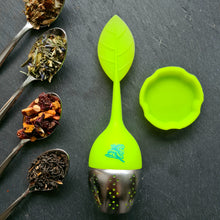 Lade das Bild in den Galerie-Viewer, Zusammengesetztes grünes Teeei mit Blattgriff und Edelstahleinsatz, daneben passende grüne Ablageschale; links daneben drei Teelöffel mit Kräuter-, Frucht- und Schwarztee-Mischungen, auf dunklem Stein.