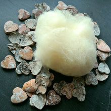 Lade das Bild in den Galerie-Viewer, Ein naturbelassener Ball aus Wolle liegt dekorativ auf einem Untergrund aus kleinen, herzförmigen Holzstücken. Die cremefarbene Schafwolle wirkt locker aufgebauscht und steht im Kontrast zu den rustikalen, braun-grauen Holzelementen.