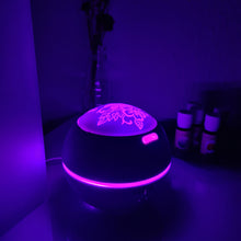 Lade das Bild in den Galerie-Viewer, Kugel-Diffusor mit floraler Gravur, violette Beleuchtung, Nachtaufnahme mit Fläschchen im Hintergrund