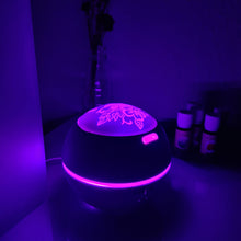 Lade das Bild in den Galerie-Viewer, Kugel-Diffusor mit floraler Gravur, violette Beleuchtung, Nachtaufnahme mit Fläschchen im Hintergrund