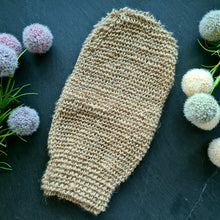 Lade das Bild in den Galerie-Viewer, Ein naturfarbener Sisal-Handschuh liegt flach auf dunklem Schieferhintergrund, umgeben von dekorativen runden Blüten in Pastelltönen. Der Handschuh hat eine grobmaschige Struktur und eine Daumenform.