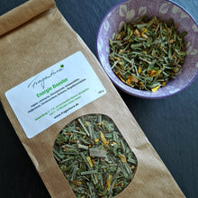 Lade das Bild in den Galerie-Viewer, Teeverpackung „Energie Booster“ von Fragantura aus braunem Papier liegt schräg neben einer violetten Porzellanschale mit der losen Teemischung aus grünlichen und gelben Pflanzenteilen.