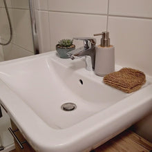 Laden und Abspielen von Videos im Galerie-Viewer, Das Video zeigt ein weißes Waschbecken und zwei Arme einer Frau, die einen Sisal-Handschuh unter dem Wasserhahn nass macht und sich die Arme damit peelt. Danach wird der Handschuh ausgewrungen und über den Waschbeckenrand gelegt.