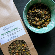 Lade das Bild in den Galerie-Viewer, Papiertüte mit Etikett „Bäuchleintee für Kinder“ neben einer Schale mit loser Kräuterteemischung; sichtbar sind Kamillenblüten, Apfelstücke, Fenchel und Melissenblätter. Die Tüte liegt schräg auf dunklem Untergrund, die Schale ist grün-weiß gemustert.