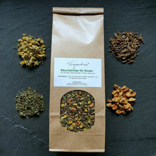 Lade das Bild in den Galerie-Viewer, Tüte „Bäuchleintee für Kinder“ mittig auf dunklem Hintergrund, umgeben von den losen Zutaten: Kamillenblüten oben links, Melissenblätter unten links, Fenchelsamen oben rechts, Apfelstücke unten rechts. Die Zutaten des Tees sind in der Sichtöffnung der Tüte gut erkennbar.