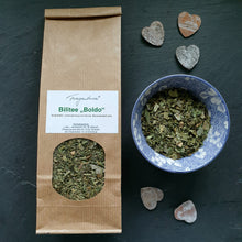 Lade das Bild in den Galerie-Viewer, Verpackung mit Sichtfenster der Kräuterteemischung „Bilitee Boldo“ von Fragantura, daneben eine dekorative blau-weiße Teeschale mit Teeblättern und drei kleinen Dekoherzen aus Holz auf dunklem Untergrund.