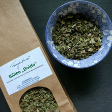 Lade das Bild in den Galerie-Viewer, Papiertüte mit weißem Etikett der Marke „Fragantura“ mit der Aufschrift „Bilitee Boldo“, daneben eine hellblaue Schale mit floraler Verzierung, gefüllt mit losem Kräutertee.