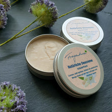 Lade das Bild in den Galerie-Viewer, Auf einer dunklen Schieferplatte stehen zwei runde Metalldosen der Marke Fragantura. Eine Dose ist geöffnet und zeigt die hellbeige Deocreme mit cremiger Textur. Die andere Dose ist geschlossen und trägt ein beigefarbenes Etikett mit der Aufschrift: „Fragantura – Natürliche Deocreme – kräuterfrisch. Cremen, statt sprühen.“ Die Szene ist mit violetten Blüten und grünen Stielen dekoriert, die der natürlichen Pflegeästhetik entsprechend.