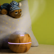 Lade das Bild in den Galerie-Viewer, Holzfarbener Kugel-Diffusor mit Sternenprojektion, Dampfausstoß, im Kinderzimmer neben Kuscheltier auf Sternenkissen