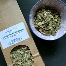 Lade das Bild in den Galerie-Viewer, Nahaufnahme einer braunen Kraftpapier-Teepackung mit dem Etikett „Fühl dich leicht-Kräutertee“ von Fragantura. Daneben steht eine lila Schale mit grünlich-bunten Kräuterbestandteilen wie Blättern und Blüten.
