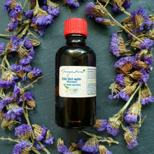 Lade das Bild in den Galerie-Viewer, Braune Glasflasche mit rotem Deckel, etikettiert mit der Aufschrift "Fühl dich wohl – Massageöl für Mutti und Kind" der Marke Fragantura. Das Produkt liegt auf dunklem Untergrund, umgeben von violetten Trockenblumen.“