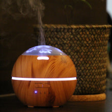 Lade das Bild in den Galerie-Viewer, Aromadiffusor in heller Holzoptik mit floraler Leuchtkuppel und sichtbarem Dampfausstoß, Pflanzkorb im Hintergrund