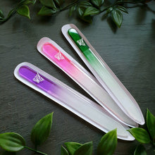 Lade das Bild in den Galerie-Viewer, Drei Glasnagelfeilen in den Farben Violett, Rosa und Grün, jeweils mit Farbverlauf zu Weiß, Liliengravur und transparenter Hülle, diagonal angeordnet auf schwarzem Hintergrund mit grüner Blätterdekoration.