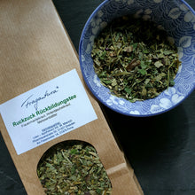 Lade das Bild in den Galerie-Viewer, Braune Papiertüte mit der Aufschrift "Fragantura Ruckzuck Rückbildungstee", daneben eine blaue Schale mit losem Kräutertee, drumherum etwas Tee verstreut.