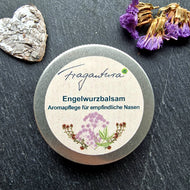 Engelwurzbalsam von Fragantura in geöffneter Runddose mit Etikett, auf dem die Aufschrift „Engelwurzbalsam – Aromapflege für empfindliche Nasen“ zu sehen ist; dekoriert mit getrockneten Blüten und einem kleinen Herz aus Naturmaterial.