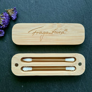 Eine geöffnete Bambusbox zeigt zwei wiederverwendbare Wattestäbchen mit weißen Silikonspitzen. Das obere Stäbchen hat eine glatte Spitze, das untere eine genoppte Struktur. Der Deckel mit dem „Fragantura“-Logo liegt darüber.