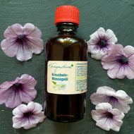 Braune Glasflasche mit rotem Schraubverschluss, darauf ein Etikett mit der Aufschrift „Fragantura Kreuzbein-Massageöl“. Die Flasche ist mittig auf dunklem Untergrund platziert, umgeben von sechs violett-weiß geaderten Blüten, die gleichmäßig um das Produkt arrangiert sind.